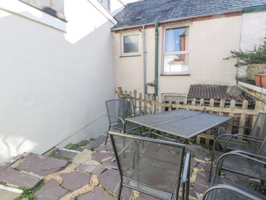 An outdoor patio area with a metal table and four metal chairs on a stone paved floor at Snowdon View in Llanberis