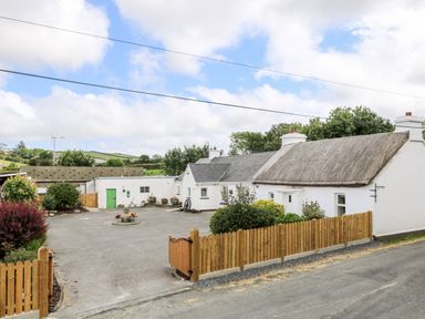 A traditional white house with a thatched roof and wooden fence surrounding a concrete driveway at Whispering Willows - The Thatch in Carndonagh County Donegal