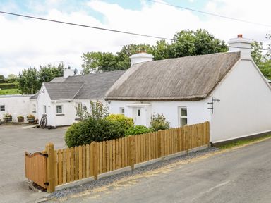 A white house with a thatched roof and a wooden fence in the front at Whispering Willows - The Thatch in Carndonagh County Donegal