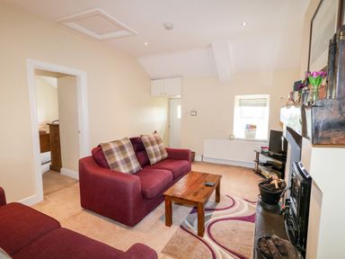 A living room with two sofas a wooden coffee table a fireplace a TV and a small window at Whispering Willows - The Thatch in Carndonagh County Donegal
