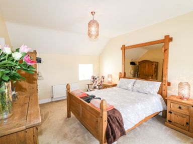 A bedroom with a wooden bed frame a floral armchair wooden furniture and a vase with flowers at Whispering Willows - The Thatch in Carndonagh County Donegal