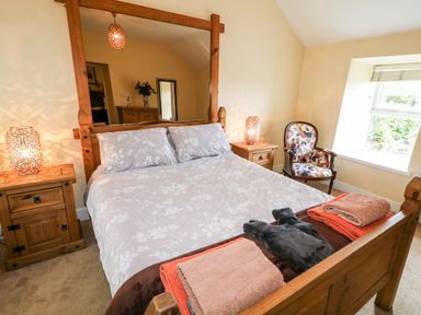 A bedroom with a wooden bed a chair a dresser and bedside tables with lamps at Whispering Willows - The Thatch in Carndonagh County Donegal