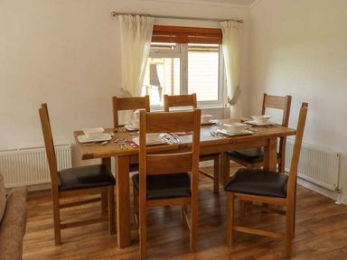 A dining room with a wooden table set for six and wooden chairs at Morgan Lodge in Hewish near Weston-super-Mare