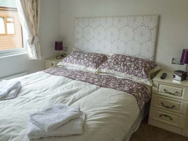 A bedroom with a double bed pillows and linens on bed two bedside tables with lamps and folded towels on bed at Morgan Lodge in Hewish near Weston-super-Mare