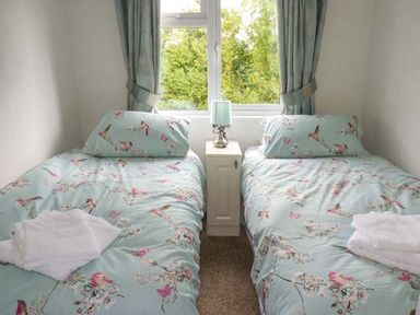 A bedroom with two single beds with floral bedding and a window with curtains at Morgan Lodge in Hewish near Weston-super-Mare