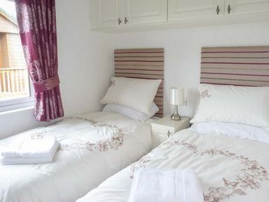 A bedroom with two single beds a nightstand with lamp and a window with curtains at Morgan Lodge in Hewish near Weston-super-Mare