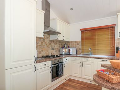 A kitchen with cream cabinets brown countertops a stove oven microwave and window blinds at Harvester Lodge in Hewish near Weston-super-Mare