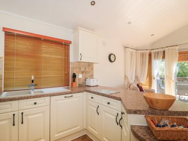 A kitchen with white cabinets a countertop a sink a wooden bowl and a basket with food items at Harvester Lodge in Hewish near Weston-super-Mare