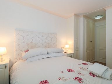 A bedroom with a bed with floral bedding bedside tables with lamps and built in wardrobes at Harvester Lodge in Hewish near Weston-super-Mare