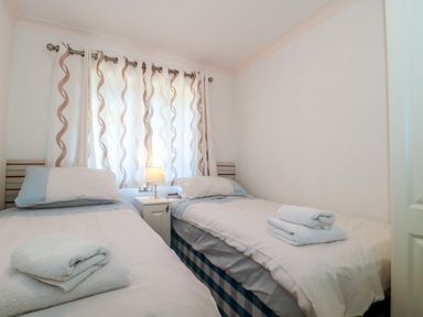 A bedroom with two single beds with white bedding and folded towels at Harvester Lodge in Hewish near Weston-super-Mare