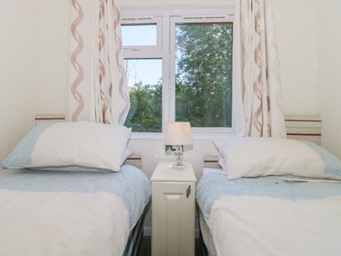 A bedroom with two single beds and a small bedside table with a lamp between them at Harvester Lodge in Hewish near Weston-super-Mare