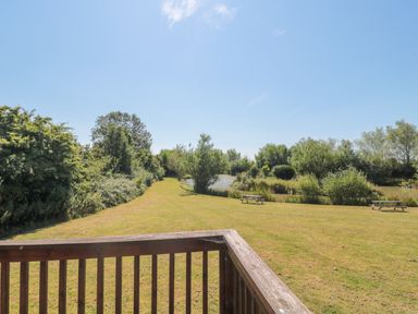 A grassy garden area with wooden benches near a pond and trees at Harvester Lodge in Hewish near Weston-super-Mare