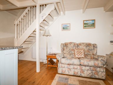 A living area with a floral sofa a wooden side table a floor lamp a staircase and framed pictures on the wall at The Ark Cottage in St Blazey