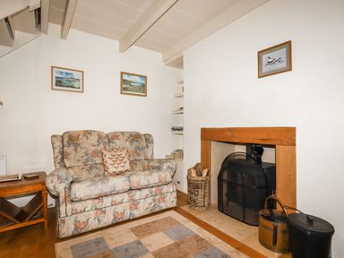 A living room with a floral sofa next to a wooden fireplace and side table at The Ark Cottage in St Blazey