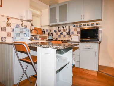 A kitchen with a granite countertop island and a wooden folding chair at The Ark Cottage in St Blazey