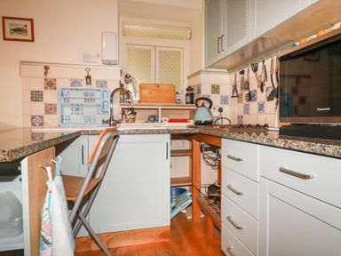 A kitchen with cabinets a countertop a microwave a kettle utensils hanging on the wall and a folding chair at The Ark Cottage in St Blazey
