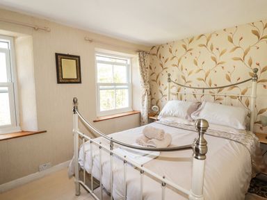 A bedroom with a bed with white metal frame and folded towels on it by two windows at The Ark Cottage in St Blazey