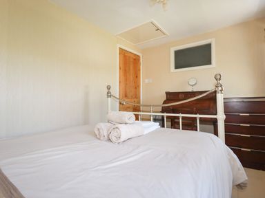 A bedroom with a bed and rolled towels on it a wooden door a chest of drawers and a desk with a mirror at The Ark Cottage in St Blazey