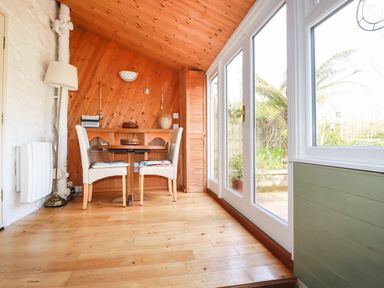 A dining area with wooden floor wooden walls table two chairs and large windows at The Ark Cottage in St Blazey