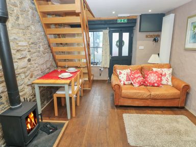 A living room with a wood stove wooden staircase dining table and brown leather sofa at Stable Cottage in Pembroke