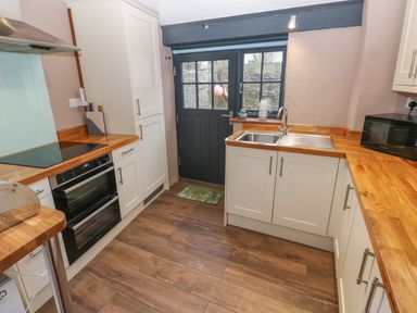 A kitchen with white cabinets wooden countertops a black oven a sink and a black door at Stable Cottage in Pembroke