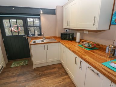 A kitchen with wooden countertops white cabinets a stainless steel sink a microwave and a door with window panes at Stable Cottage in Pembroke
