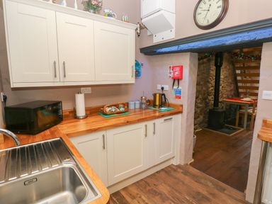 A kitchen with white cabinets wooden countertops a stainless steel sink a microwave and a kettle at Stable Cottage in Pembroke