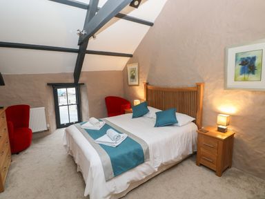 A bedroom with a double bed and wooden headboard two red armchairs a wooden chest of drawers and bedside tables with lamps at Stable Cottage in Pembroke
