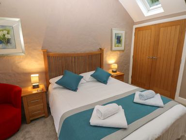 A bedroom with a double bed with blue pillows and towels on it flanked by wooden nightstands with lamps a red chair and wooden double doors at Stable Cottage Pembroke