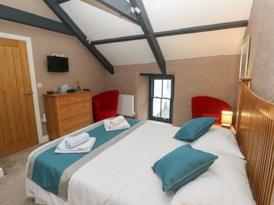 A bedroom with a bed with blue pillows two red armchairs a wooden dresser a small wall-mounted TV and exposed ceiling beams at Stable Cottage in Pembroke