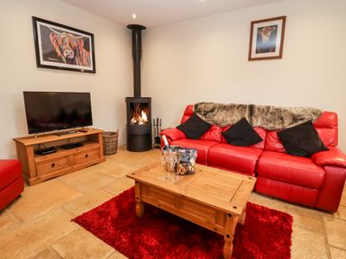 A living room with a red leather sofa wooden coffee table and a television at Cow Byre in Great Tew near Chipping Norton