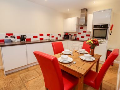 A kitchen with white cabinets red and white tiled backsplash wooden table set with dishes and red chairs at Cow Byre Great Tew near Chipping Norton