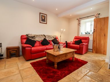 A living room with red leather sofa and armchair wooden coffee table and red rug at Cow Byre in Great Tew near Chipping Norton