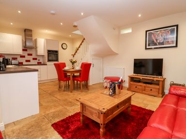 An open-plan living room and kitchen with red chairs and sofa at Cow Byre in Great Tew near Chipping Norton