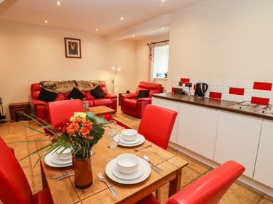 A living room with red leather sofas and a dining table with flowers and white dishes at Cow Byre Great Tew near Chipping Norton