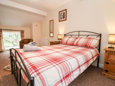 A bedroom with a double bed with red plaid bedding a chair and two wooden nightstands with lamps at Cow Byre Great Tew near Chipping Norton