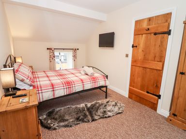 A bedroom with a double bed with checkered bedding a wooden door and a television on the wall at Cow Byre Great Tew near Chipping Norton