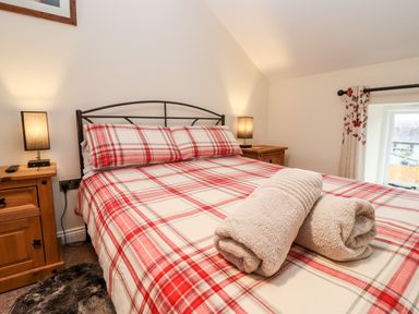 A bedroom with a bed with red and white checkered bedding and two rolled towels at Cow Byre Great Tew near Chipping Norton