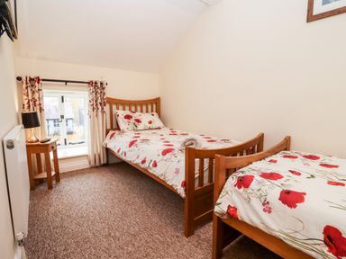 A bedroom with two single beds with floral bedding and a window with curtains at Cow Byre Great Tew near Chipping Norton