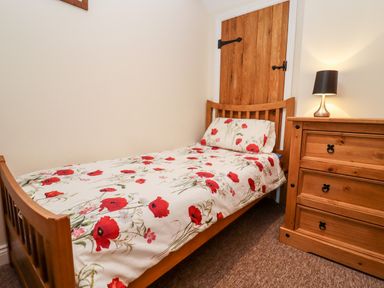 A bedroom with a wooden single bed with floral bedding a wooden dresser and a lamp at Cow Byre Great Tew near Chipping Norton