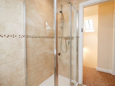 A bathroom with a glass shower enclosure and beige tiled walls at Cow Byre Great Tew near Chipping Norton