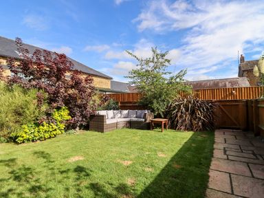 A backyard with outdoor seating a wooden table plants and a paved walkway at Cow Byre in Great Tew near Chipping Norton
