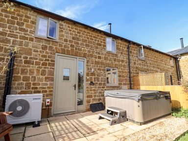 A stone exterior wall with grey door and windows next to a covered hot tub and a Samsung air conditioning unit at Cow Byre Great Tew near Chipping Norton