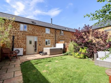 A garden with green grass a wooden bench a hot tub and outdoor seating at Cow Byre Great Tew near Chipping Norton
