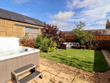A backyard with a hot tub and garden furniture on grass surrounded by plants at Cow Byre Great Tew near Chipping Norton