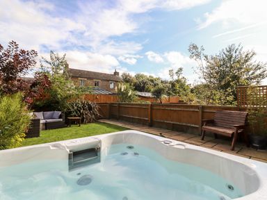 A garden with a hot tub wooden bench and outdoor sofa with cushions at Cow Byre Great Tew near Chipping Norton