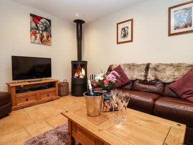 A living room with a wood burning stove leather sofa and wooden coffee table at The Stables in Great Tew near Chipping Norton