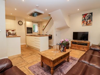 An open plan living room and kitchen with leather sofas wooden coffee table and TV at The Stables Great Tew near Chipping Norton