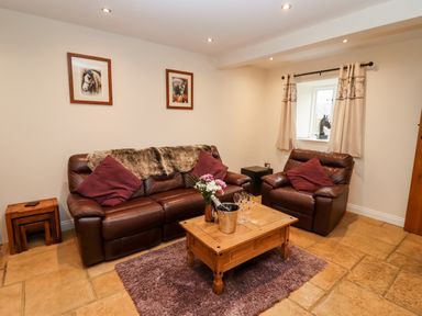 A living room with brown leather sofa and armchair a wooden coffee table with flowers and glasses on a rug at The Stables Great Tew near Chipping Norton