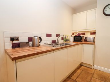 A kitchen with wooden countertop white cabinets a sink a kettle microwave toaster and a clock on the wall at The Stables Great Tew near Chipping Norton